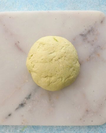 yellow color naan dough on a white square marble.