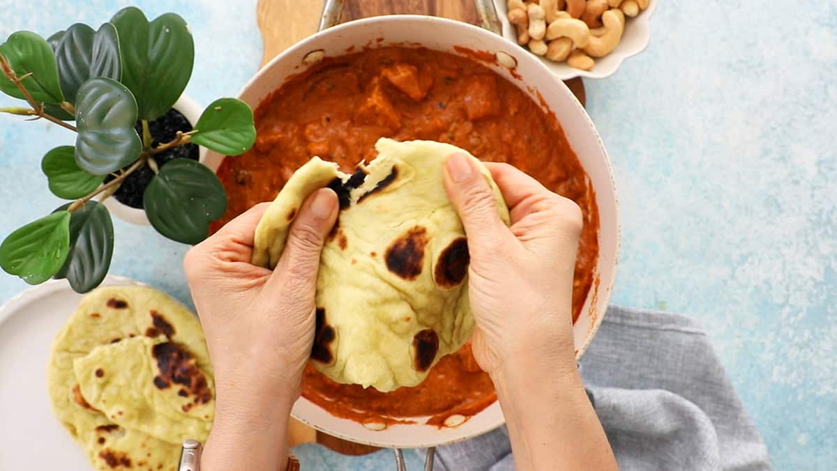 two hands tearing one naan bread.