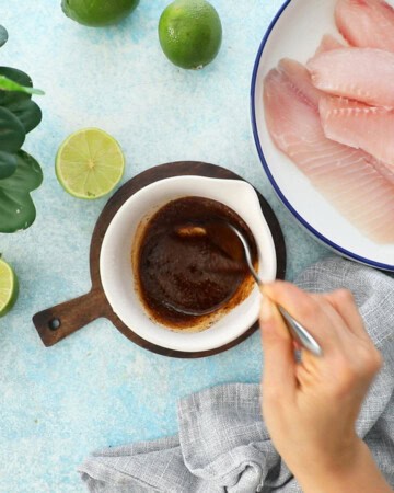 a hand mixing a brown sauce in a white bowl.