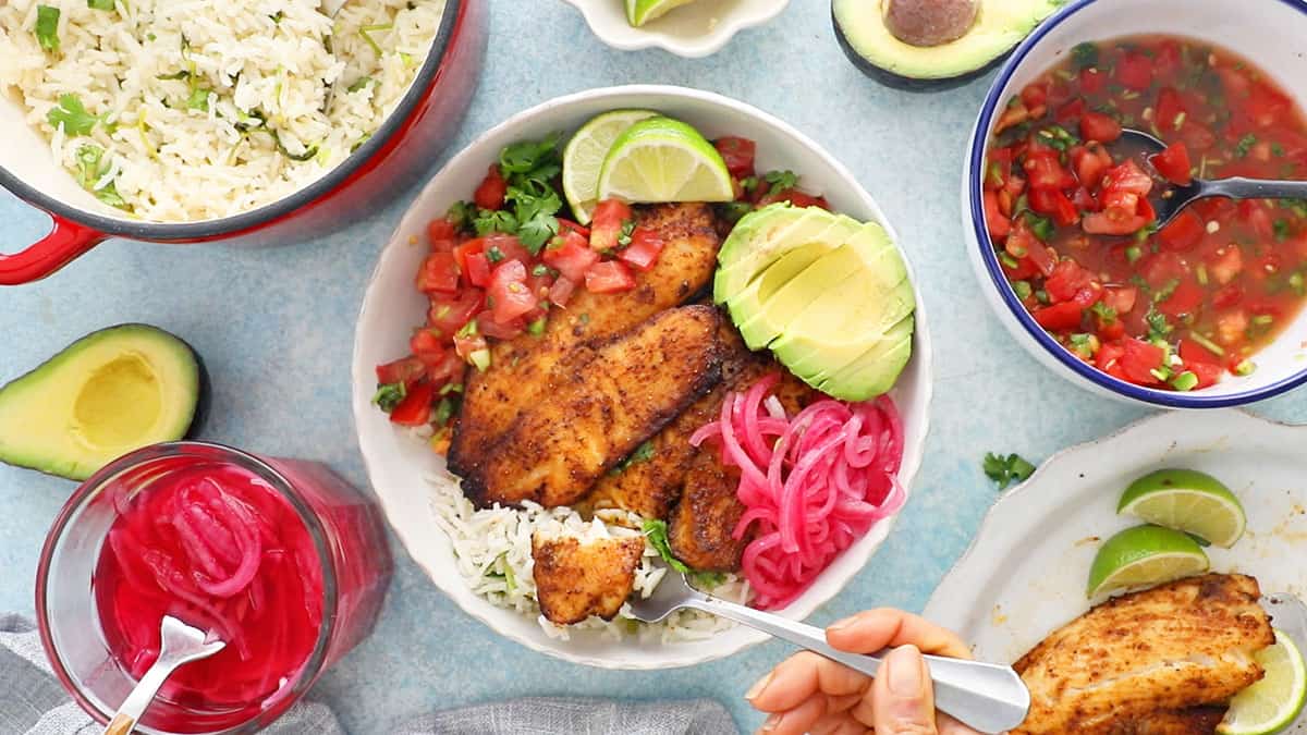 one white bowl with brown tilapia, green avocado and pink onions.