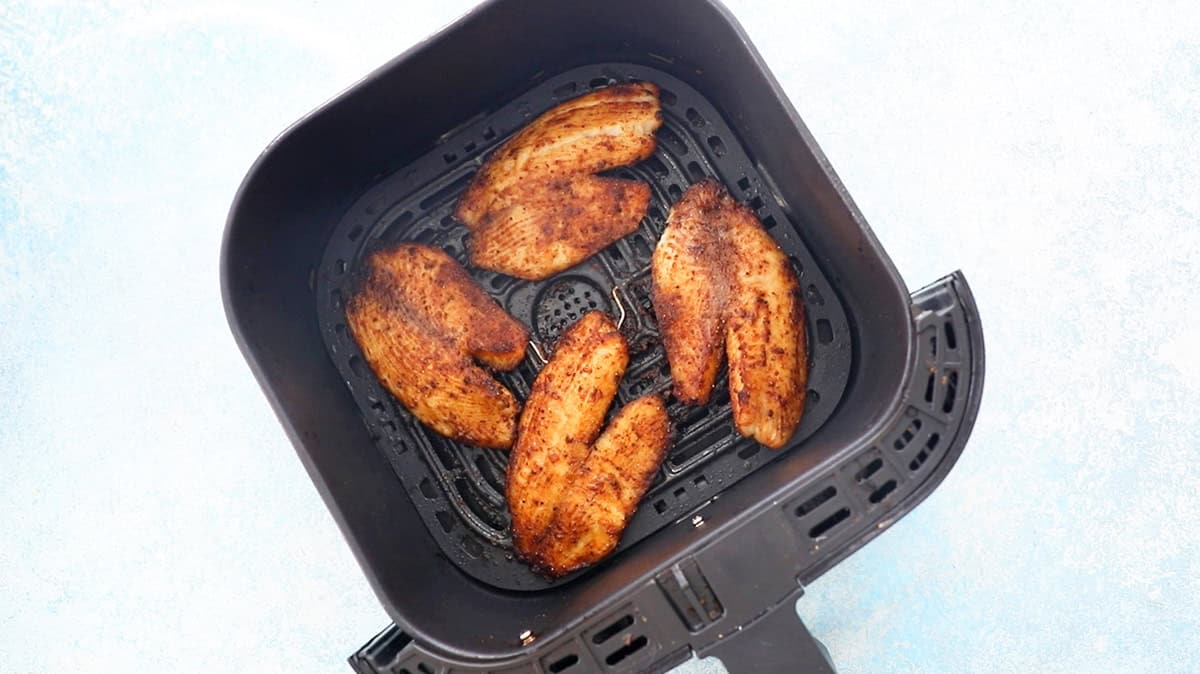 4 brown fish fillets in a black air fryer basket.