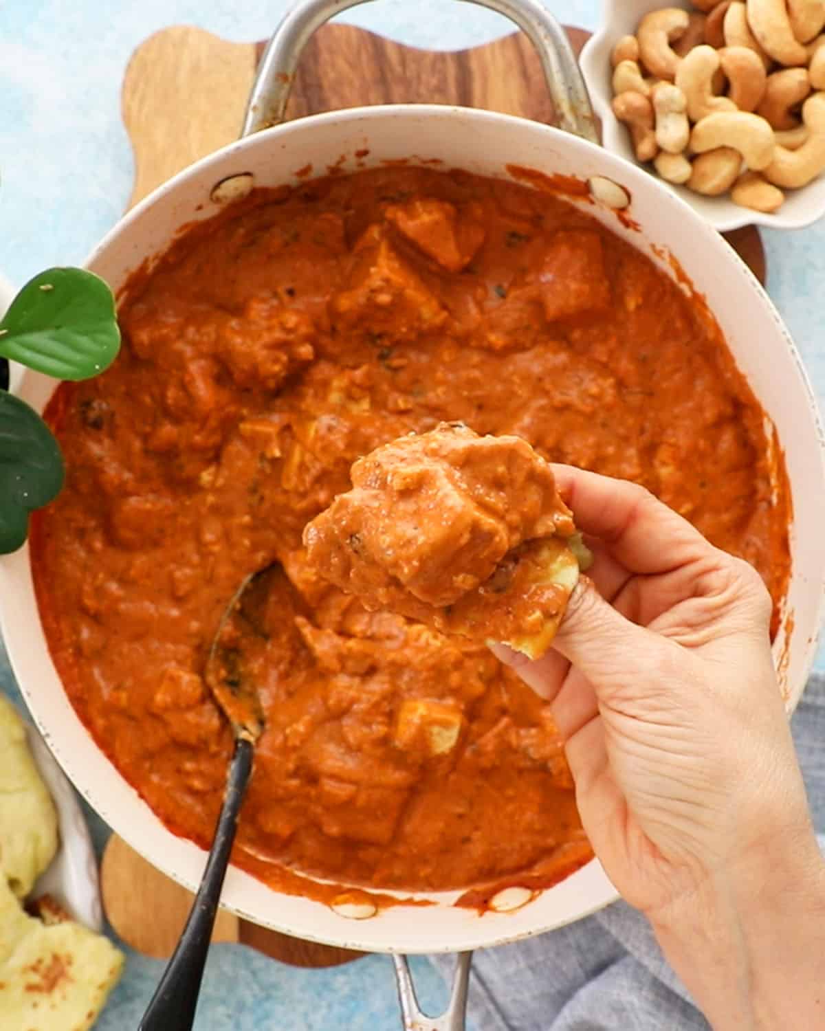 a hand holding a scoop of orange tofu tikka masala.
