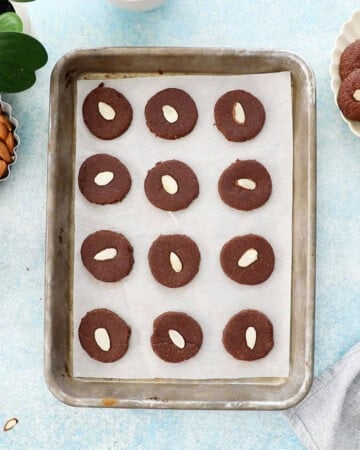 12 bron cookie dough circles in a white paper lined metal baking sheet.