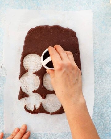 a hand cutting out circles from a brown cookie dough.