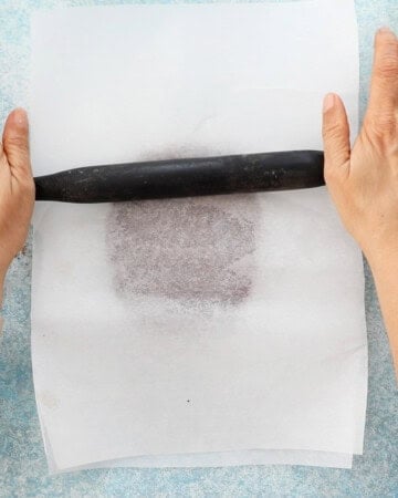 two hands rolling brown cookie dough on a white paper.