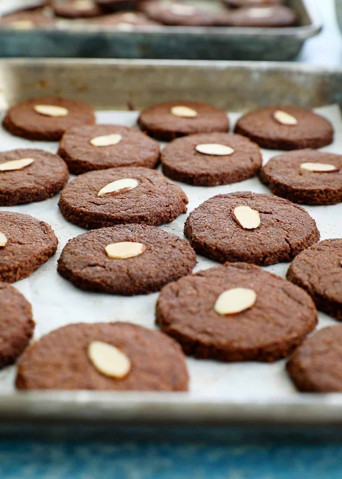 brown almond flour chocolate cookies on a white paper lined metal baking sheet.