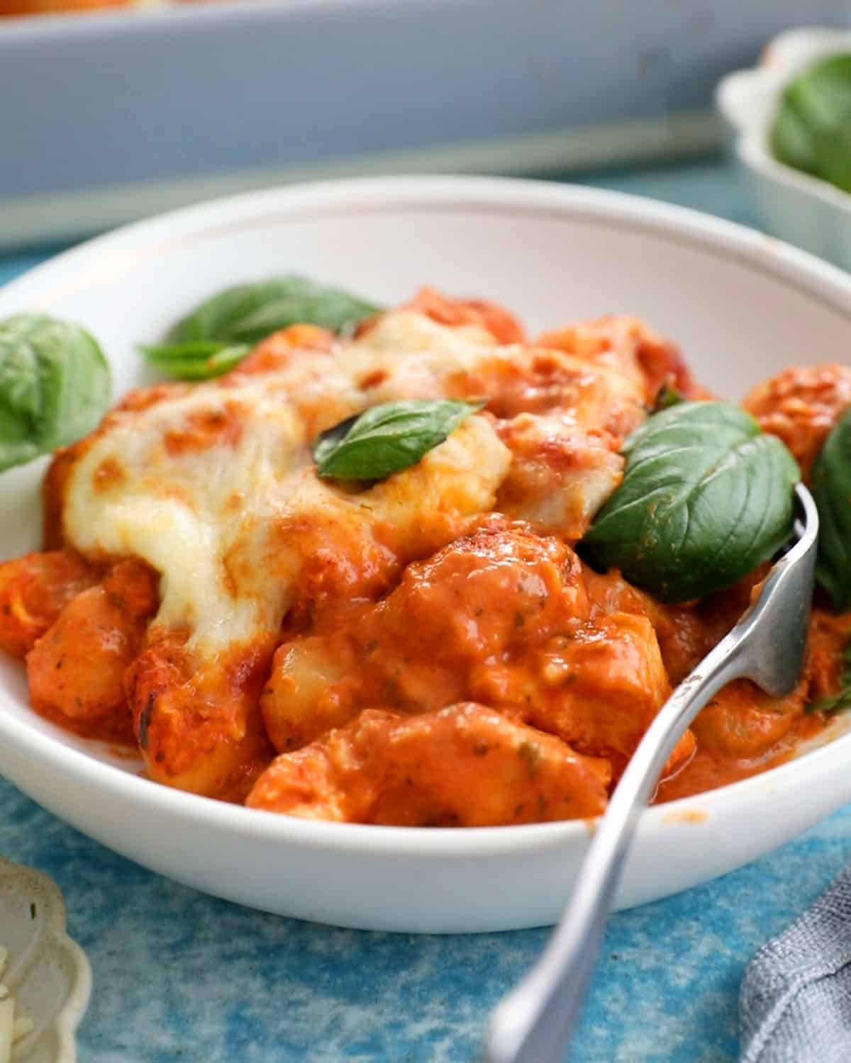 orange and white gnocchi and chicken in a white bowl with green basil.