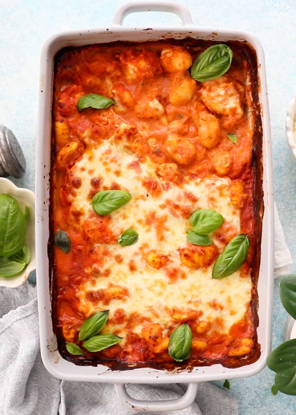 orange and white gnocchi and chicken in a grey baking dish with green basil.