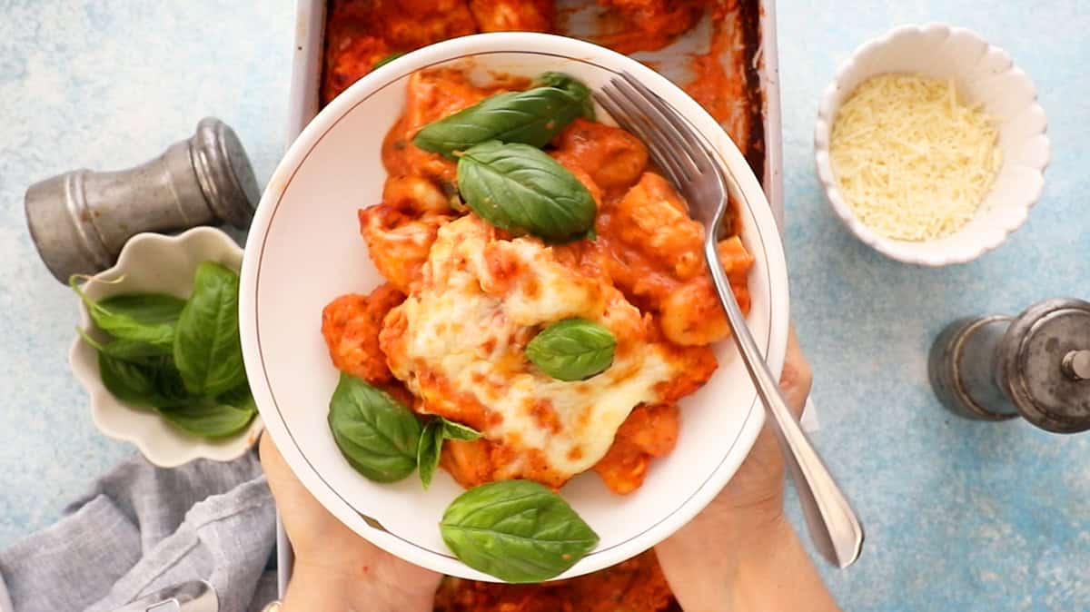 orange and white gnocchi and chicken in a white bowl with green basil.