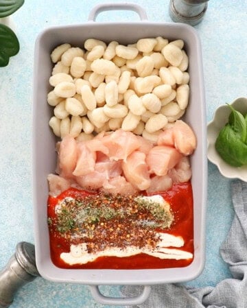 orange and white gnocchi and chicken in a grey baking dish.
